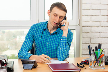 Image showing Specialist in the office talking on the phone in preparation for recording information