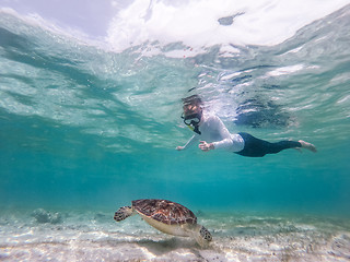 Image showing Woman on vacations wearing snokeling mask swimming with sea turtle in turquoise blue water of Gili islands, Indonesia. Underwater photo.