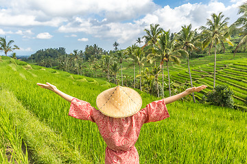 Image showing Relaxed fashionable caucasian woman wearing red asian style kimono and traditional asian paddy hat, arms rised to sky, enjoying pure nature at beautiful green rice fields on Bali island