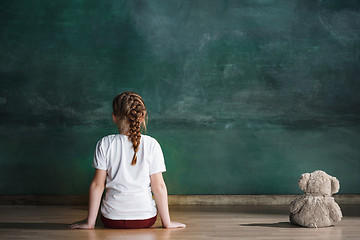 Image showing Little girl with teddy bear sitting on floor in empty room. Autism concept