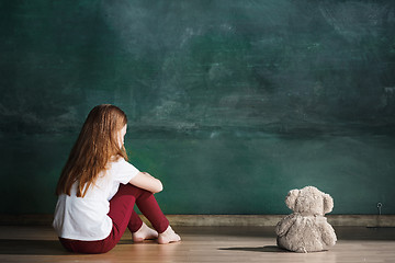 Image showing Little girl with teddy bear sitting on floor in empty room. Autism concept