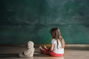 Image showing Little girl with teddy bear sitting on floor in empty room. Autism concept