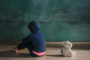 Image showing Little girl with teddy bear sitting on floor in empty room. Autism concept