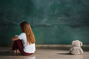 Image showing Little girl with teddy bear sitting on floor in empty room. Autism concept