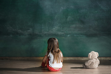 Image showing Little girl with teddy bear sitting on floor in empty room. Autism concept