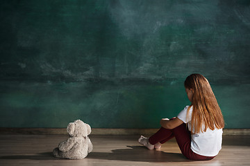 Image showing Little girl with teddy bear sitting on floor in empty room. Autism concept