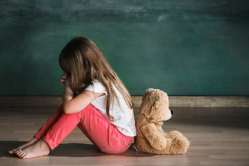 Image showing Little girl with teddy bear sitting on floor in empty room. Autism concept