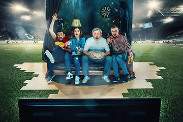 Image showing Soccer football fans sitting on the sofa and watching TV in the middle of a football field.