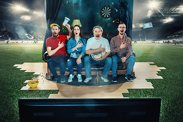 Image showing Soccer football fans sitting on the sofa and watching TV in the middle of a football field.