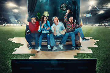 Image showing Soccer football fans sitting on the sofa and watching TV in the middle of a football field.