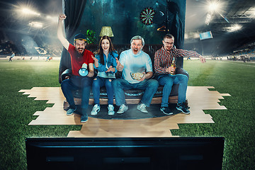 Image showing Soccer football fans sitting on the sofa and watching TV in the middle of a football field.