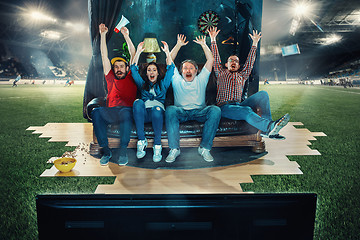 Image showing Soccer football fans sitting on the sofa and watching TV in the middle of a football field.