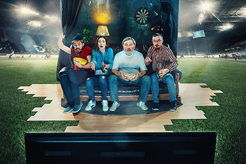 Image showing Soccer football fans sitting on the sofa and watching TV in the middle of a football field.