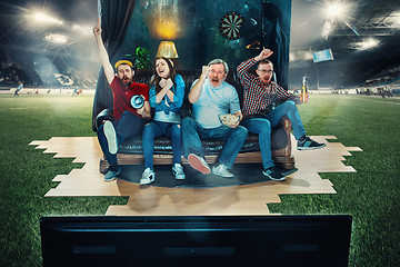 Image showing Soccer football fans sitting on the sofa and watching TV in the middle of a football field.