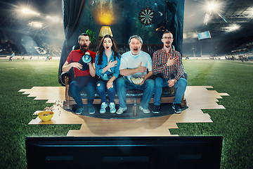 Image showing Soccer football fans sitting on the sofa and watching TV in the middle of a football field.