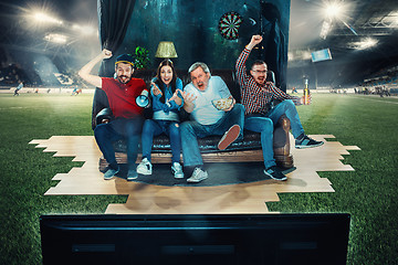 Image showing Soccer football fans sitting on the sofa and watching TV in the middle of a football field.