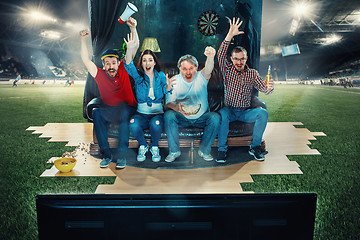 Image showing Soccer football fans sitting on the sofa and watching TV in the middle of a football field.