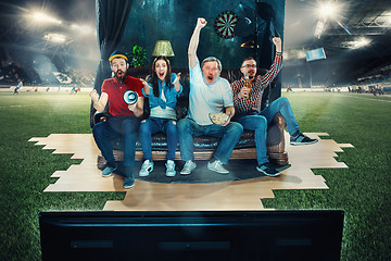 Image showing Soccer football fans sitting on the sofa and watching TV in the middle of a football field.