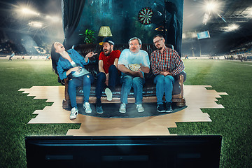 Image showing Soccer football fans sitting on the sofa and watching TV in the middle of a football field.