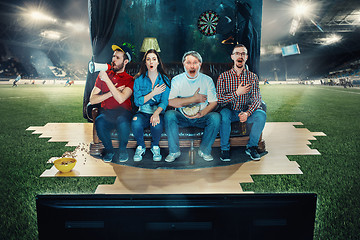 Image showing Soccer football fans sitting on the sofa and watching TV in the middle of a football field.