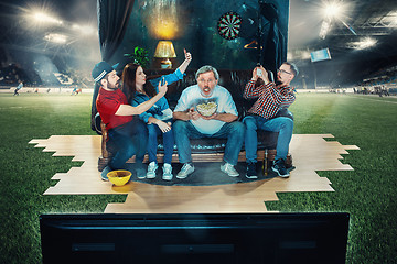 Image showing Soccer football fans sitting on the sofa and watching TV in the middle of a football field.