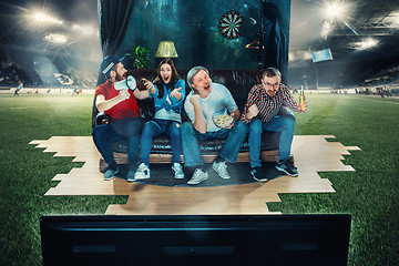 Image showing Soccer football fans sitting on the sofa and watching TV in the middle of a football field.