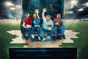 Image showing Soccer football fans sitting on the sofa and watching TV in the middle of a football field.