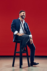 Image showing The happy business man sitting and smiling against red background.