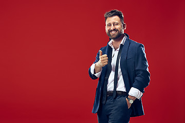 Image showing The happy business man standing and smiling against red background.