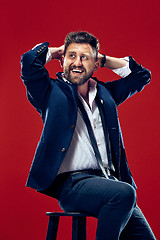 Image showing The happy business man sitting and smiling against red background.