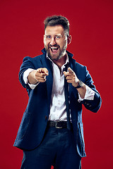 Image showing The happy business man point you and want you, half length closeup portrait on red background.