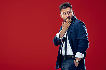 Image showing The young man whispering a secret behind her hand over red background