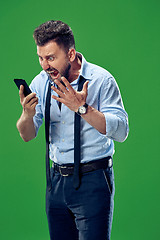 Image showing The young emotional angry man screaming on green studio background