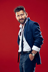 Image showing Male beauty concept. Portrait of a fashionable young man with stylish haircut wearing trendy suit posing over red background.