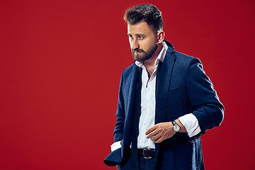 Image showing Male beauty concept. Portrait of a fashionable young man with stylish haircut wearing trendy suit posing over red background.