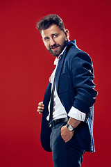 Image showing Male beauty concept. Portrait of a fashionable young man with stylish haircut wearing trendy suit posing over red background.