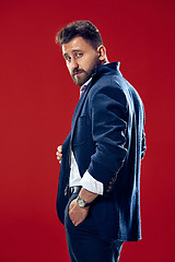 Image showing Male beauty concept. Portrait of a fashionable young man with stylish haircut wearing trendy suit posing over red background.