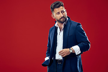 Image showing Male beauty concept. Portrait of a fashionable young man with stylish haircut wearing trendy suit posing over red background.