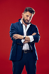 Image showing Male beauty concept. Portrait of a fashionable young man with stylish haircut wearing trendy suit posing over red background.