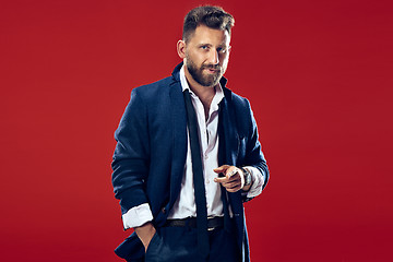 Image showing Male beauty concept. Portrait of a fashionable young man with stylish haircut wearing trendy suit posing over red background.