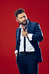 Image showing Male beauty concept. Portrait of a fashionable young man with stylish haircut wearing trendy suit posing over red background.