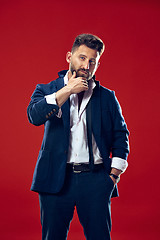 Image showing Male beauty concept. Portrait of a fashionable young man with stylish haircut wearing trendy suit posing over red background.