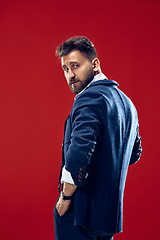 Image showing Male beauty concept. Portrait of a fashionable young man with stylish haircut wearing trendy suit posing over red background.