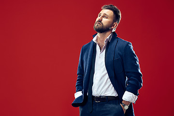 Image showing Male beauty concept. Portrait of a fashionable young man with stylish haircut wearing trendy suit posing over red background.