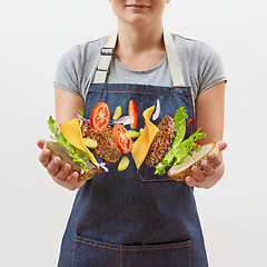 Image showing Female chef in a denim apron with flying tasty homemade burger from fresh natural ingredients in her hands on a white background. Place for text.