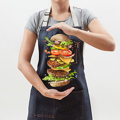 Image showing Big homemade fresh burger in the girl\'s hands from flying ingredients - fresh vegetables and organic natural beef meat on a white background.