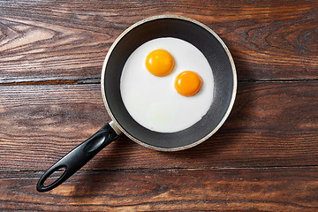 Image showing Fried eggs in a frying pan on a wooden background with copy space. Breakfast from natural fresh products. Top view.