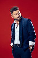 Image showing Male beauty concept. Portrait of a fashionable young man with stylish haircut wearing trendy suit posing over red background.