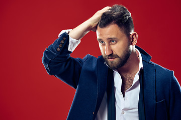 Image showing Male beauty concept. Portrait of a fashionable young man with stylish haircut wearing trendy suit posing over red background.