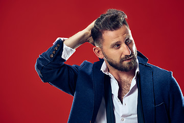 Image showing Male beauty concept. Portrait of a fashionable young man with stylish haircut wearing trendy suit posing over red background.